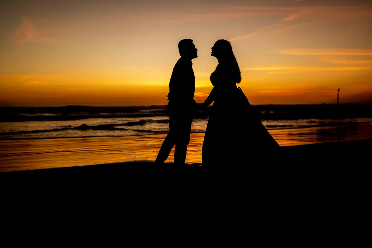 Couple in silhouette facing each other on the beach at sunset